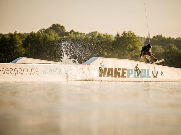 Wakeboarder auf einer beschrifteten Rampe im Süsel Seeparx